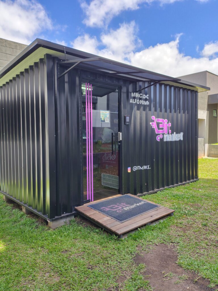 Fachada completa de uma unidade Bitmarket, mercado autonomo em container preto com porta aberta